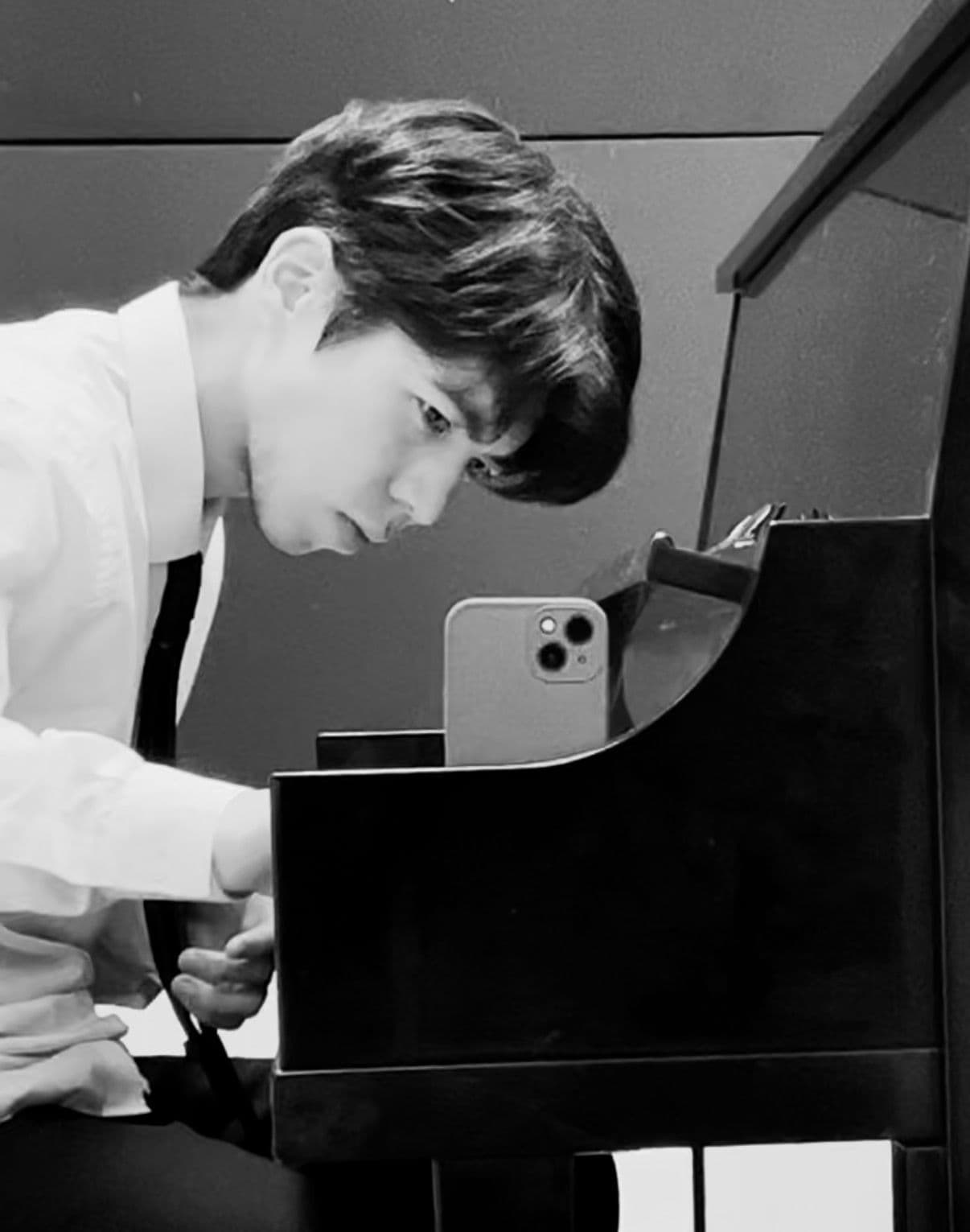 Kanat Nazarov playing piano and composing music in a studio setting, black and white portrait.